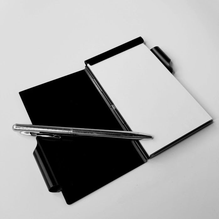 Black and white notebook with a pen on a light gray background