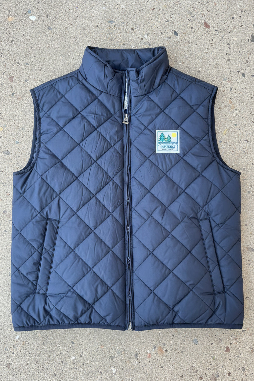 A close-up of a black blue quilted puffer vest with a silver zipper and a square Indiana-themed patch on the chest.