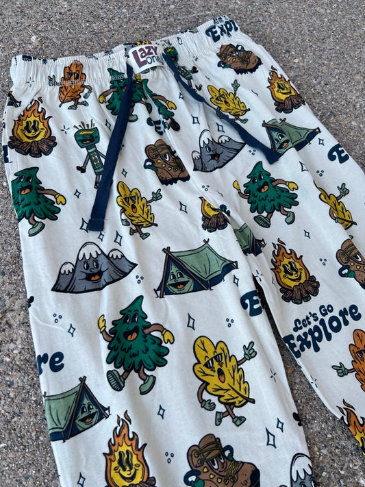 Close up of white fleece lounge pants with an all-over camping-themed print featuring tents, campfires, trees, and the words 'Go Explore', laid flat on a gray asphalt surface.