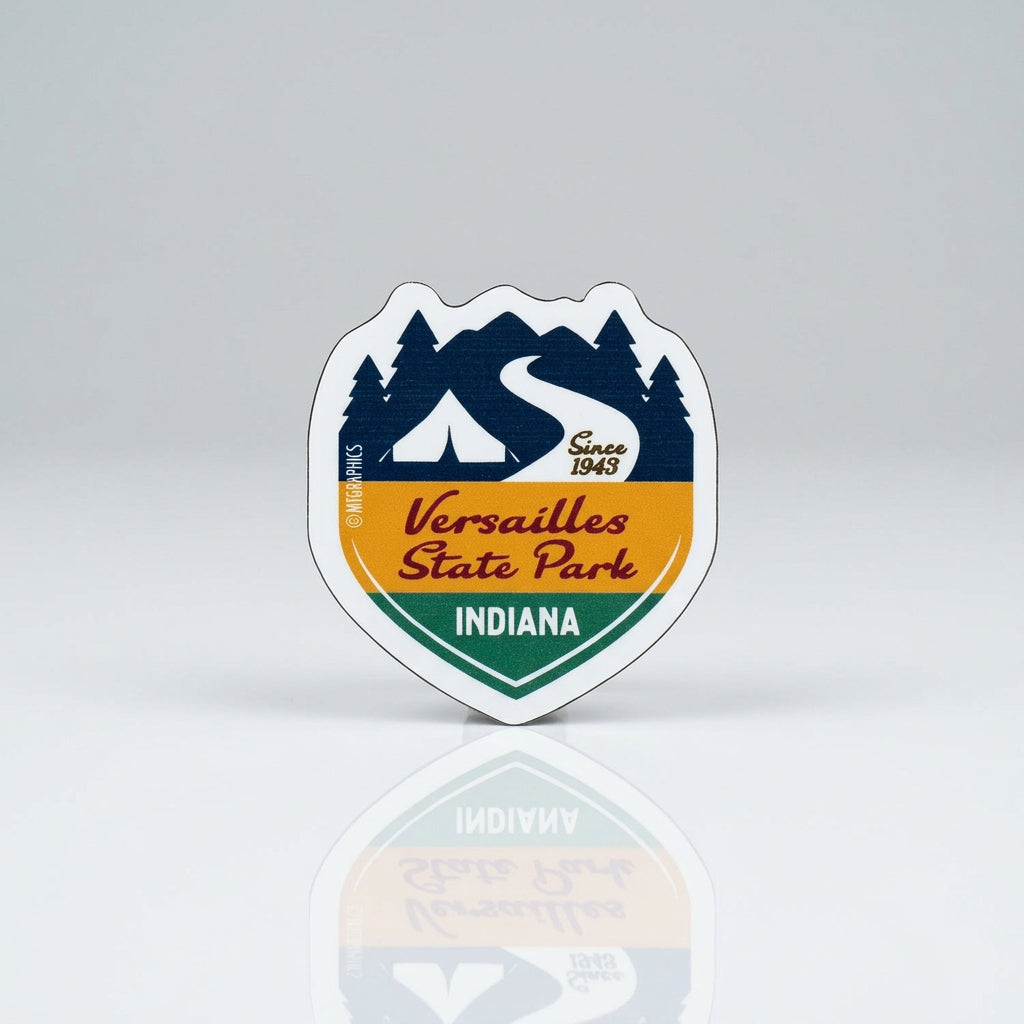 Shield‑shaped magnet with a stylized mountain and trail graphic, featuring the text “Versailles State Park,” “Indiana,” and “Since 1943.”