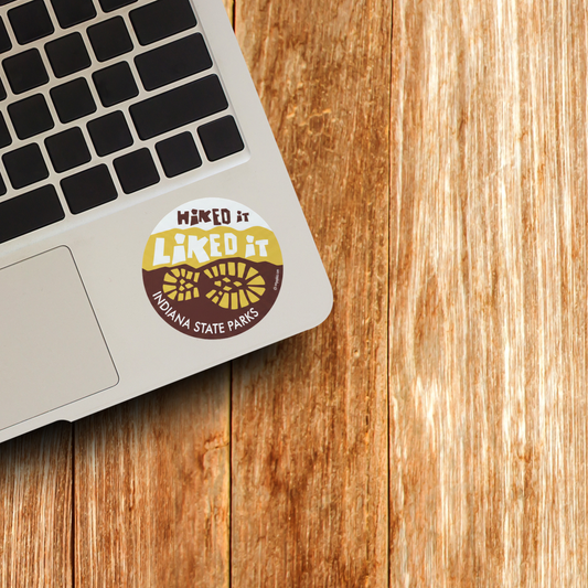 Laptop with a 'Hiked It Liked it Indiana State Parks' sticker on a wooden surface