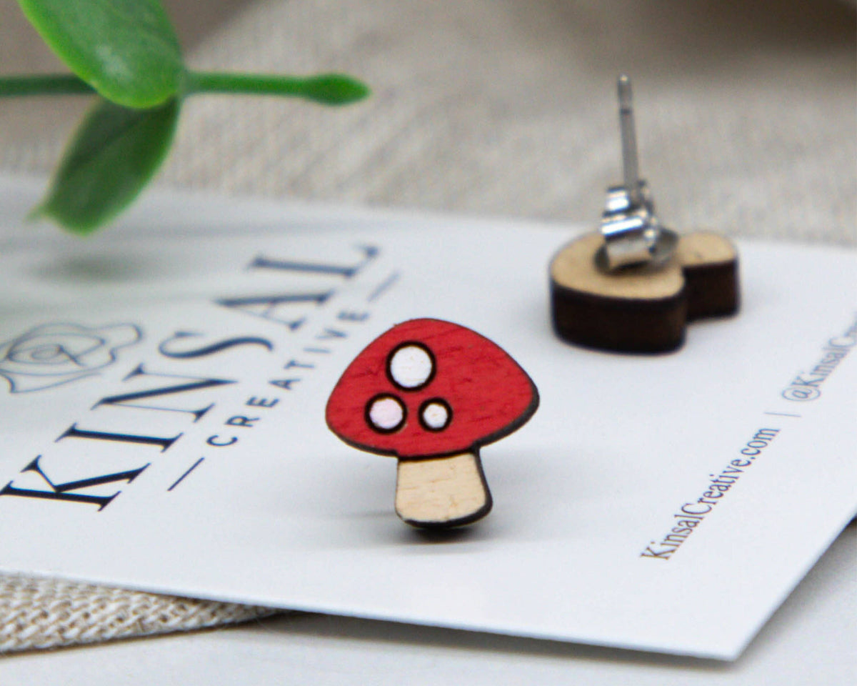 Mushroom-shaped earrings on a Kinsale Creative branded card with a plant in the background.
