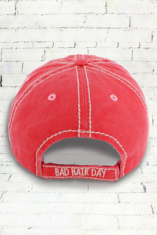 Back of a salmon pink cap with 'Bad Hair Day' text on a white brick wall background