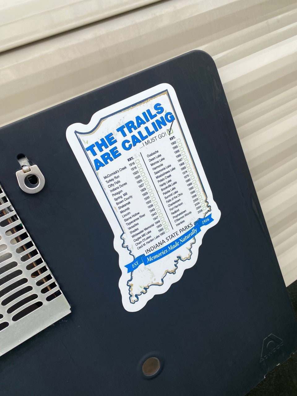 Sticker with 'The Trails Are Calling' text on a black surface