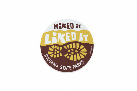 Round sticker with 'Hiked it, Liked it' text and Indiana State Parks logo on a wooden surface