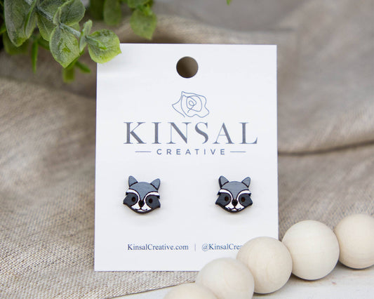 Raccoon-shaped earrings on a Kinsal Creative branded card with decorative elements.