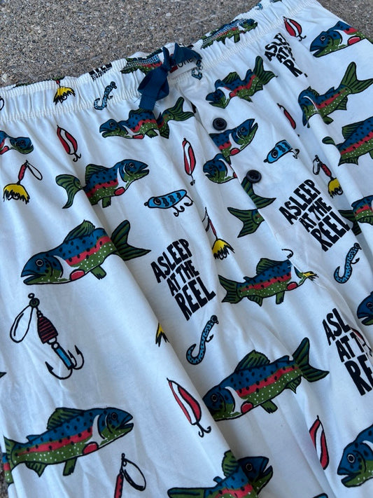 White shorts with an all-over fishing-themed print featuring colorful fish, hooks, lures, and the text 'ASLEEP AT THE REEL'.