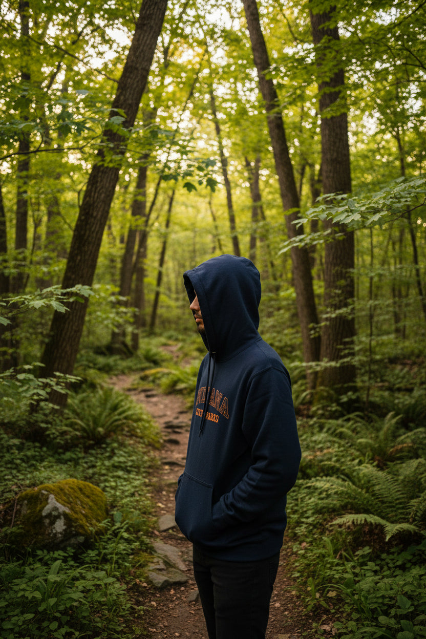 A black pullover hoodie with 'INDIANA STATE PARKS' printed in orange and camo, worn by someone in a nature scene