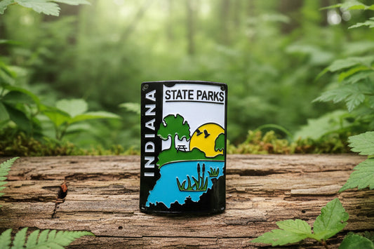 An Indiana State Parks hiking medallion featuring a landscape design with a blue lake, green trees, a yellow sun, and the words 'INDIANA STATE PARKS' in a nature scene