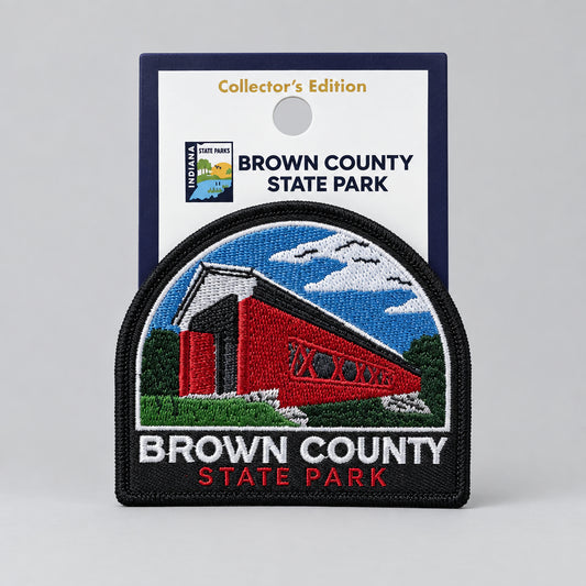 An embroidered patch of Brown County State Park featuring a red covered bridge under a blue sky, displayed in front of its dark blue Collector's Edition backing card.