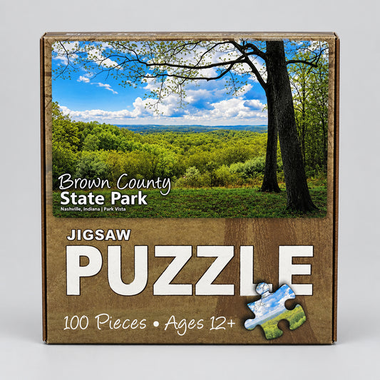 Boxed jigsaw puzzle package for Brown County State Park, showing a scenic landscape photo of green hills and trees under a blue sky, with large white text reading 'JIGSAW PUZZLE' and '100 Pieces • Ages 12+'.