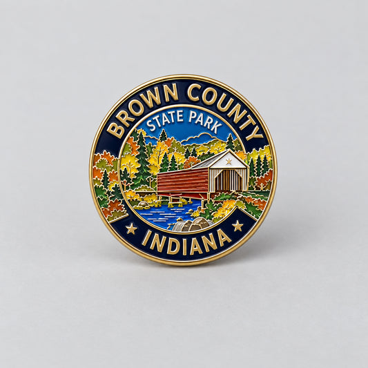 A round enamel pin featuring the Brown County State Park with a gold-tone border, blue and gold lettering, and a multicolor landscape illustration.