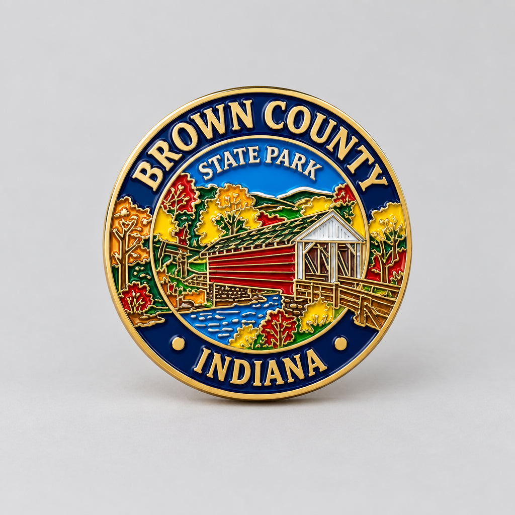 A round enamel pin featuring the Brown County State Park logo from Indiana, with a gold-tone border, blue outer ring, and a colorful central illustration of a covered bridge, autumn trees, and a river.