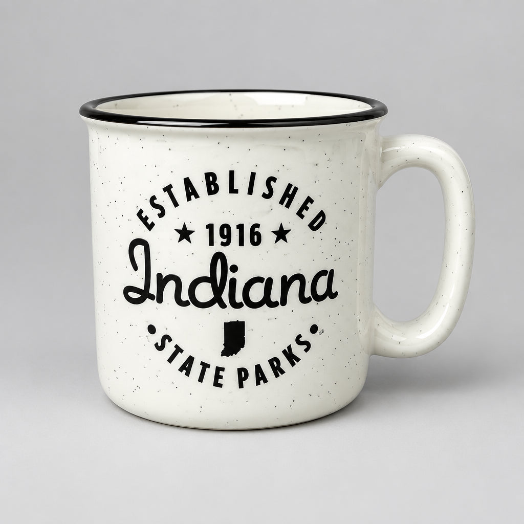A white speckled mug with a black rim and black printed text reading 'ESTABLISHED 1916 Indiana STATE PARKS' on a gray countertop.