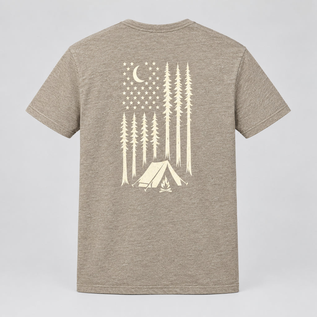 A heathered green short-sleeve t-shirt laid flat on a dark gray textured carpet, featuring a cream-colored graphic on the back with a crescent moon, stars, pine trees, and a tent.