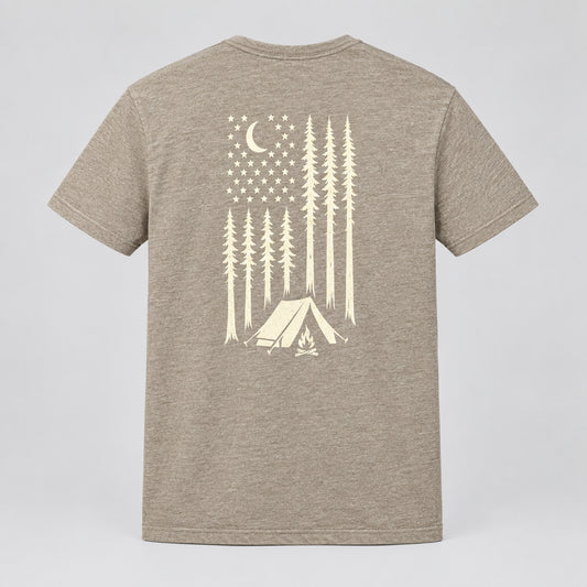 A heathered green short-sleeve t-shirt laid flat on a dark gray textured carpet, featuring a cream-colored graphic on the back with a crescent moon, stars, pine trees, and a tent.