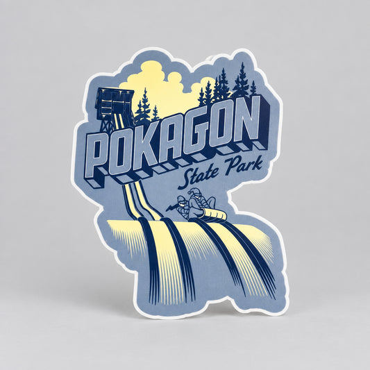 A blue sticker showing a toboggan tower, evergreen trees, and two people riding a toboggan down icy tracks, with the text “Pokagon State Park.”
