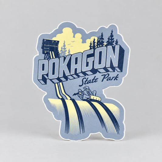 A blue sticker showing a toboggan tower, evergreen trees, and two people riding a toboggan down icy tracks, with the text “Pokagon State Park.”