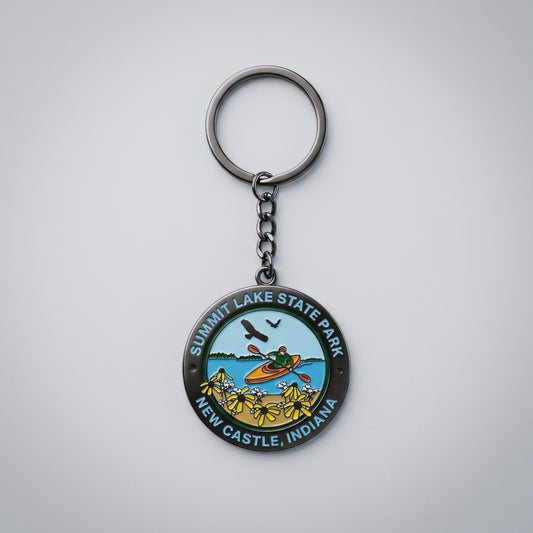 Round metal keychain showing a kayaker on a lake with wildflowers in the foreground and birds in the sky, labeled “Summit Lake State Park New Castle, Indiana.”