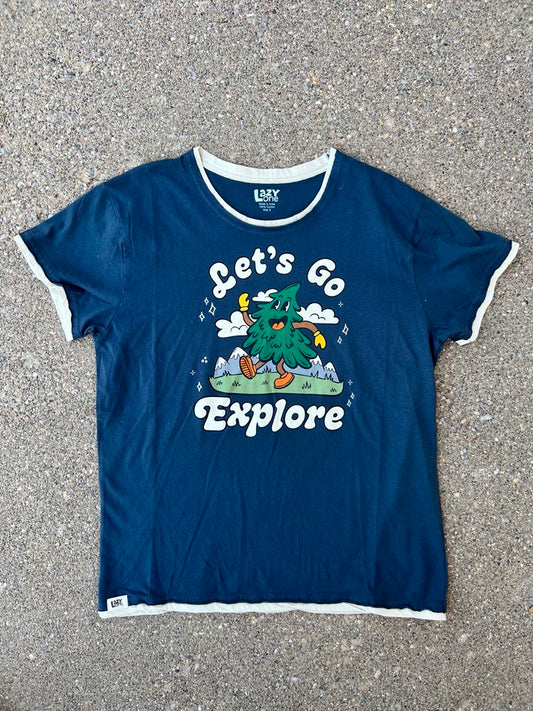 A navy blue ringer t-shirt with white trim and a colorful graphic on the front, laid flat on a gray asphalt background. The graphic features a green tree character with the text 'Let's Go Explore'.