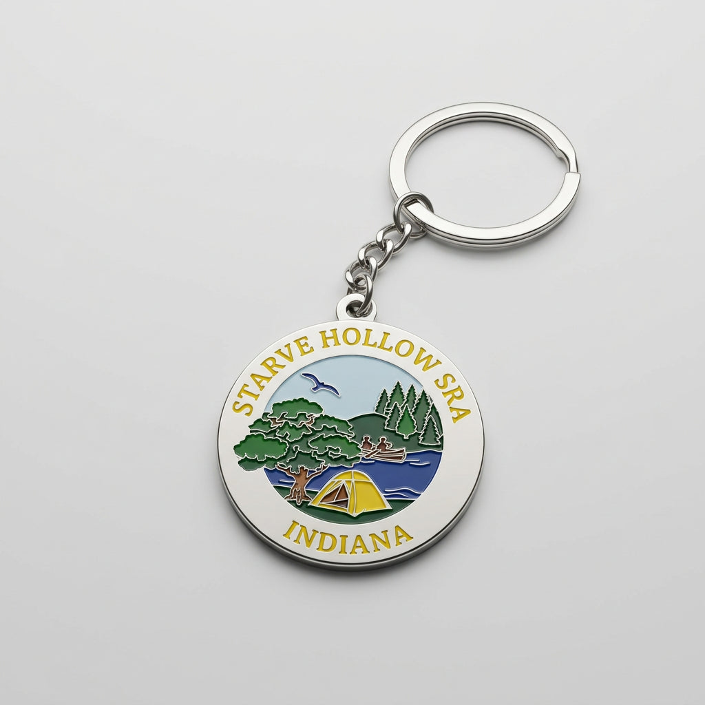Round metal keychain with an enamel scene showing a tent, trees, water, and a flying bird, labeled “Starve Hollow SRA Indiana.”