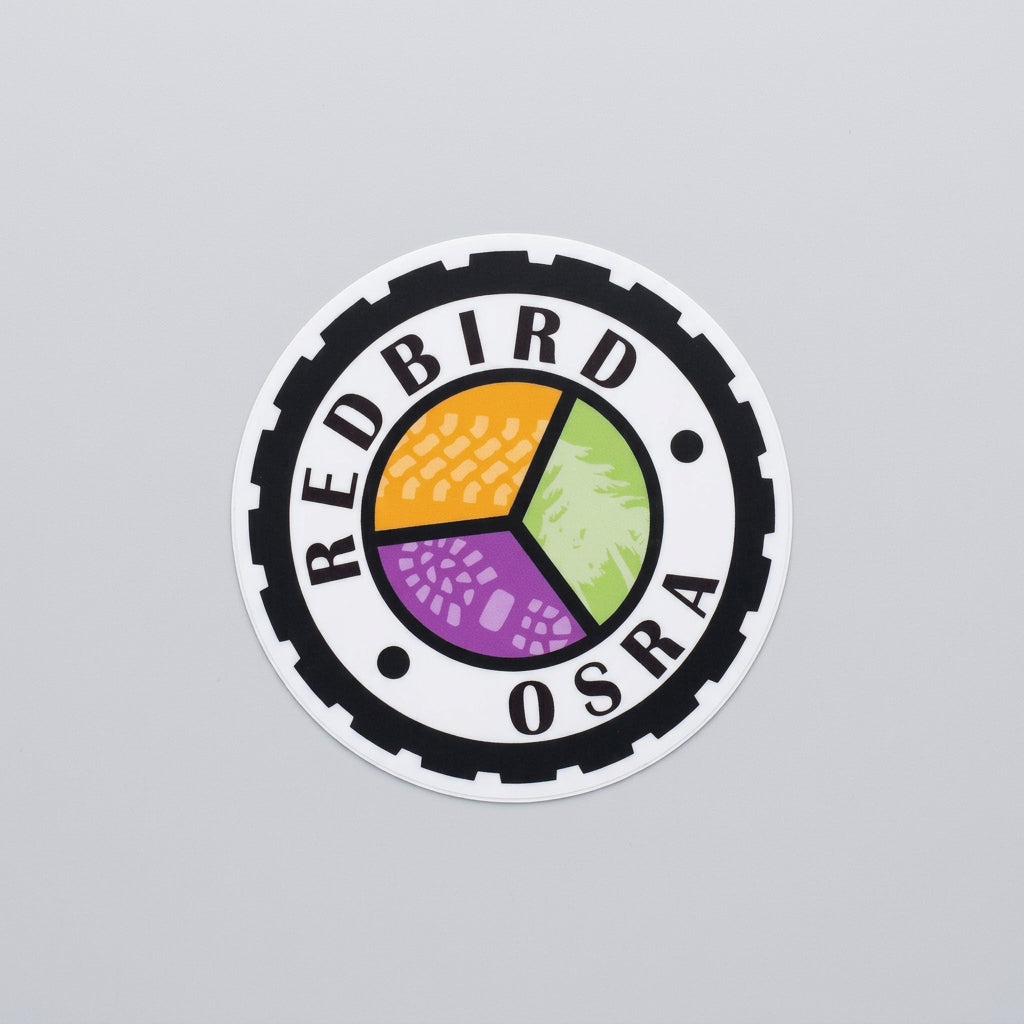 Round sticker with a black gear‑shaped border, the text “Redbird OSRA,” and a three‑color segmented center design in orange, green, and purple.