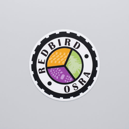 Round sticker with a black gear‑shaped border, the text “Redbird OSRA,” and a three‑color segmented center design in orange, green, and purple.