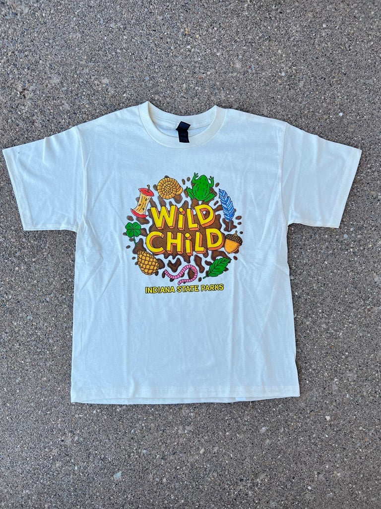 A cream short-sleeve youth t-shirt with a colorful 'Wild Child' graphic print, laid flat on a gray asphalt surface.