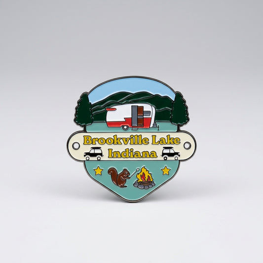 Enamel‑style hiking medallion with a camper in front of hills, cars, a squirrel, stars, and a campfire, labeled “Brookville Lake Indiana.”