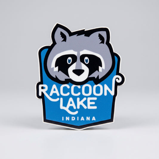 Die‑cut sticker with a stylized raccoon face above the text “Raccoon Lake Indiana” on a blue background.