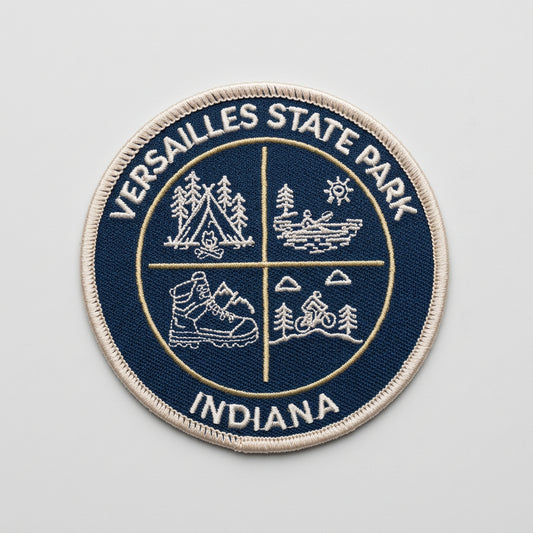 Round embroidered patch with four outdoor icons—tent, canoe, hiking boot, and bicycle—labeled “Versailles State Park Indiana.”