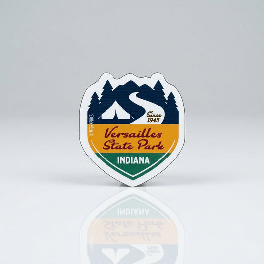 Shield‑shaped magnet with a stylized mountain and trail graphic, featuring the text “Versailles State Park,” “Indiana,” and “Since 1943.”