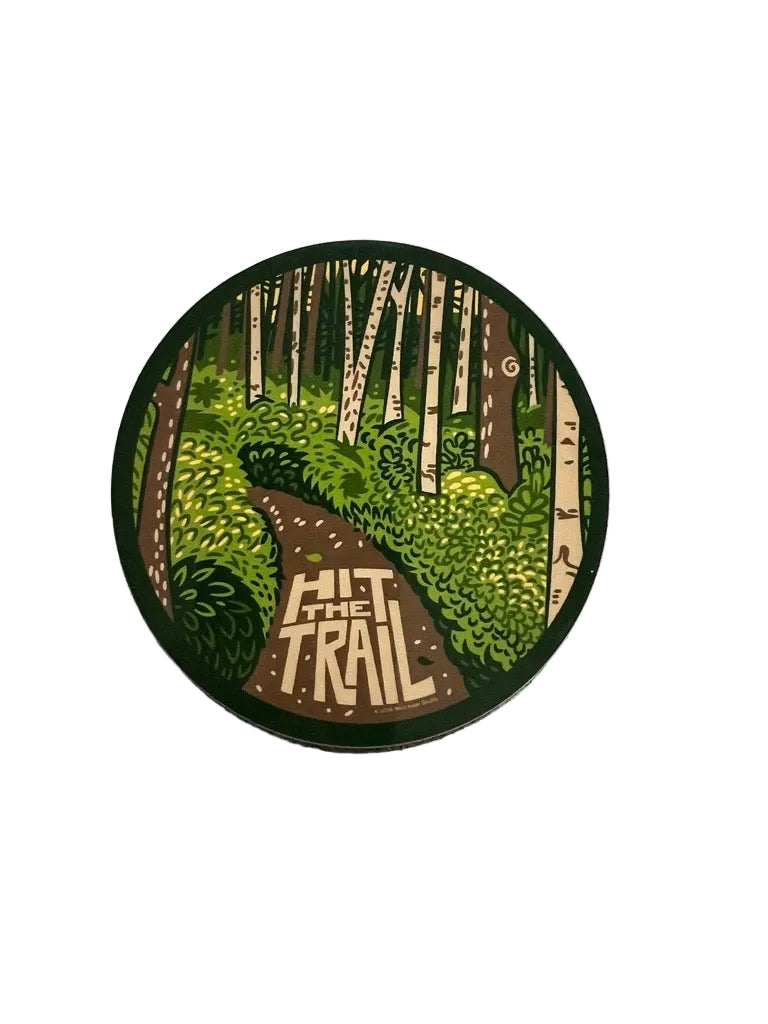 Round sticker with forest design and 'Hit the Trail' text on a textured surface