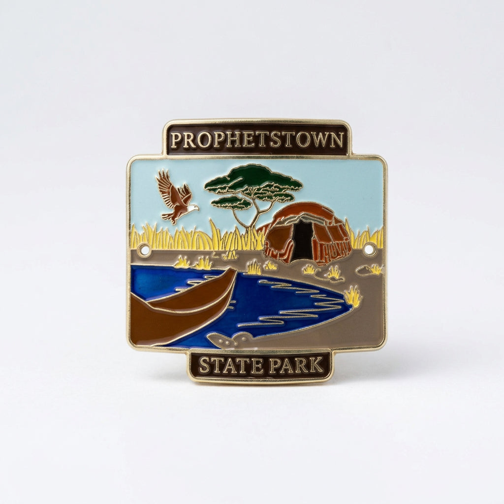 Enamel‑style hiking medallion showing a canoe on the water with tall grasses, wildlife, and a structure in the background, labeled “Prophetstown State Park.”