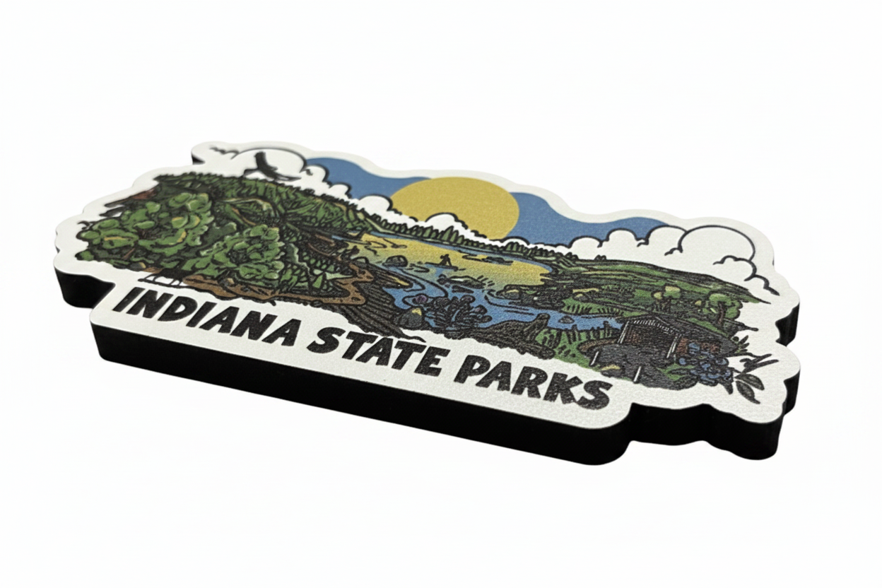 An Indiana State Parks souvenir magnet featuring a colorful landscape illustration with a yellow sun, blue sky, green trees, and a river, with the text 'INDIANA STATE PARKS' in black on a white border