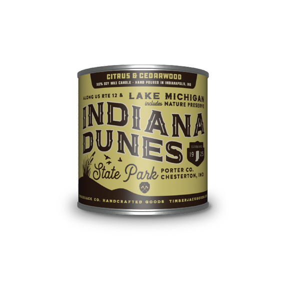A cylindrical metal tin with Indiana Dunes State Park label, Citrus and Cedarwood candle scent, featuring a tan and brown label, set against a plain white background.