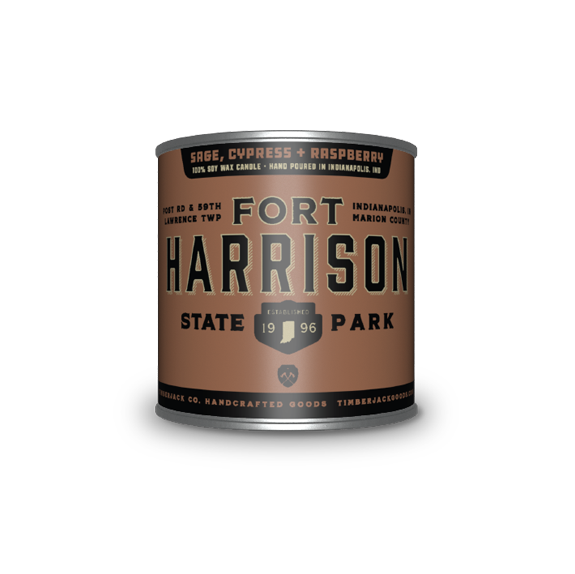 A cylindrical metal tin with Fort Harrison State Park label, Sage, Cypress, and Raspberry candle scent, featuring a brown and dark dark brown label, set against a plain white background.