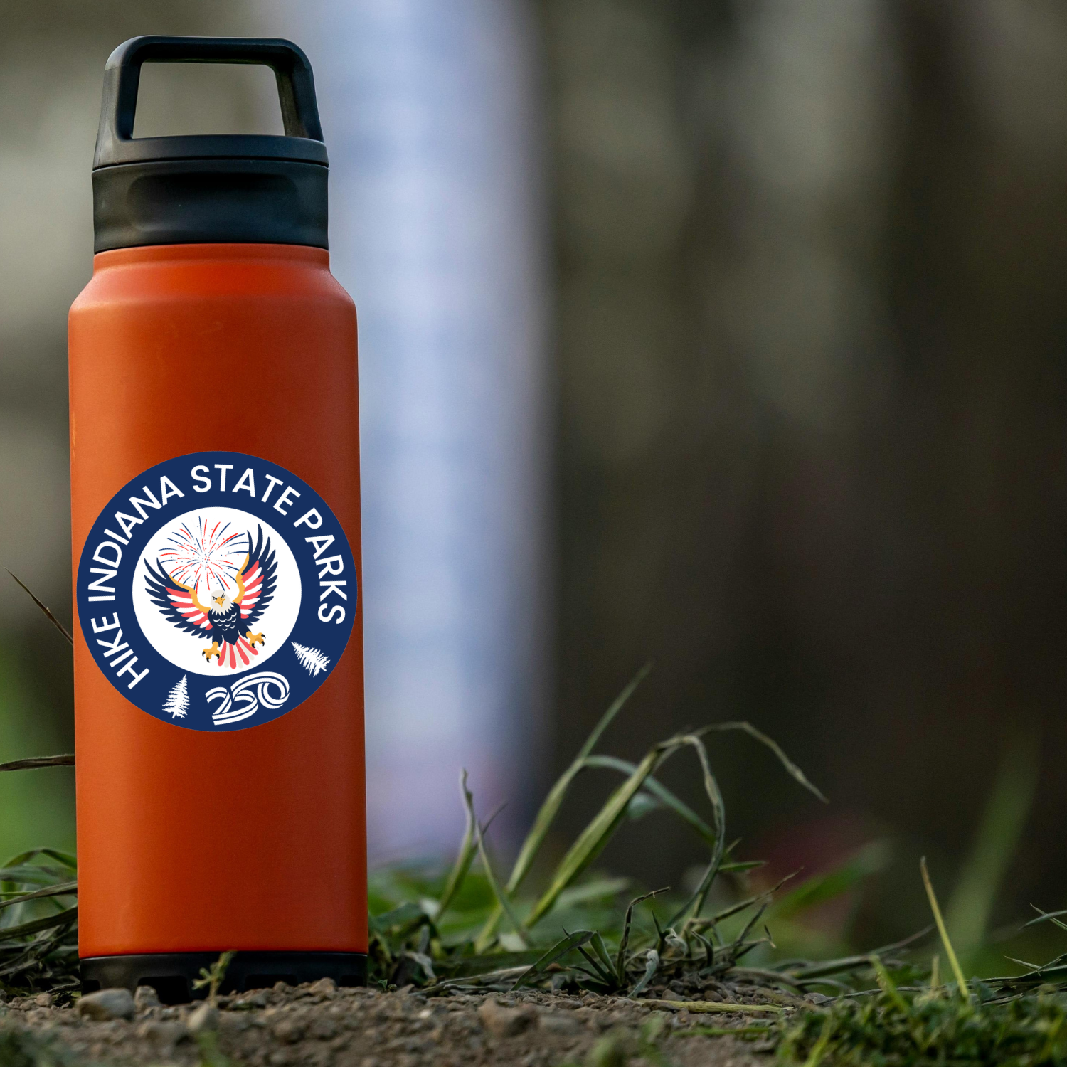 round circle that says hike indiana state parks with americas 250th logo on an orange water bottle in a forest setting