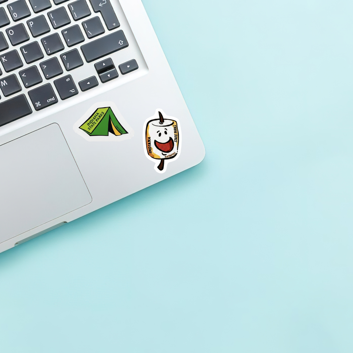 Laptop with a green tent sticker and marshmallow sticker on a light blue background