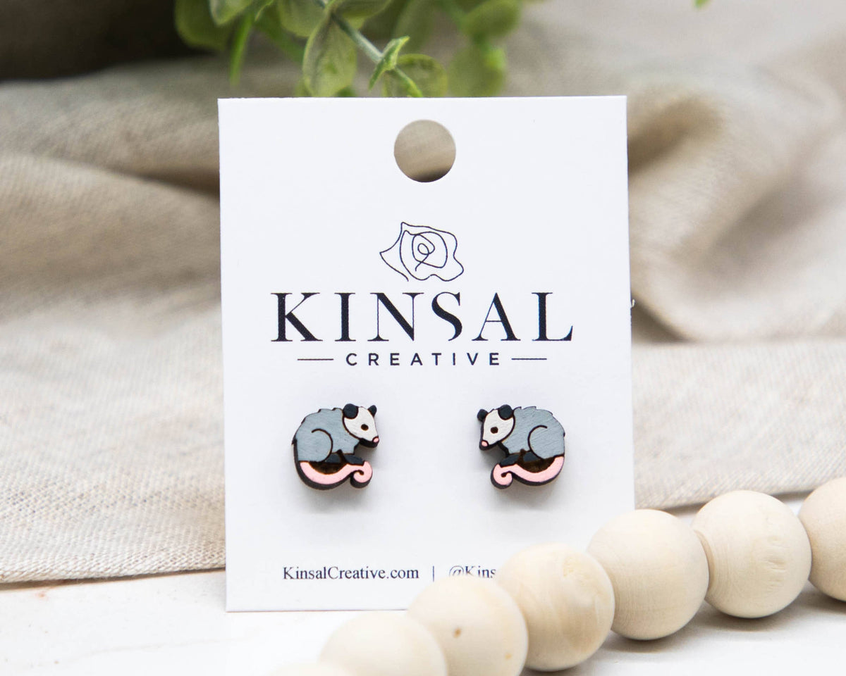 Pair of gray and pink animal-shaped earrings on a Kinsal Creative branded card with a beige fabric background.