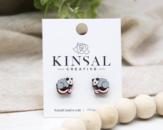 Pair of gray and pink animal-shaped earrings on a Kinsal Creative branded card with a beige fabric background.