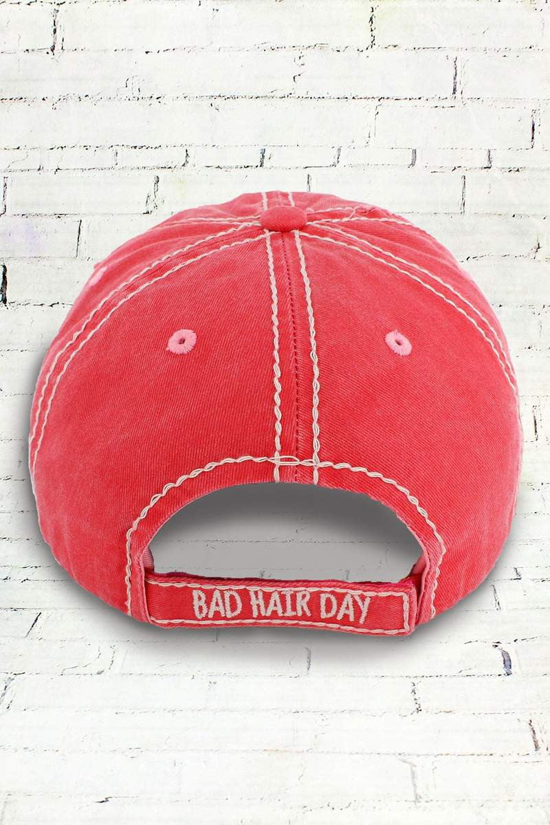 Back of a salmon pink cap with 'Bad Hair Day' text on a white brick wall background