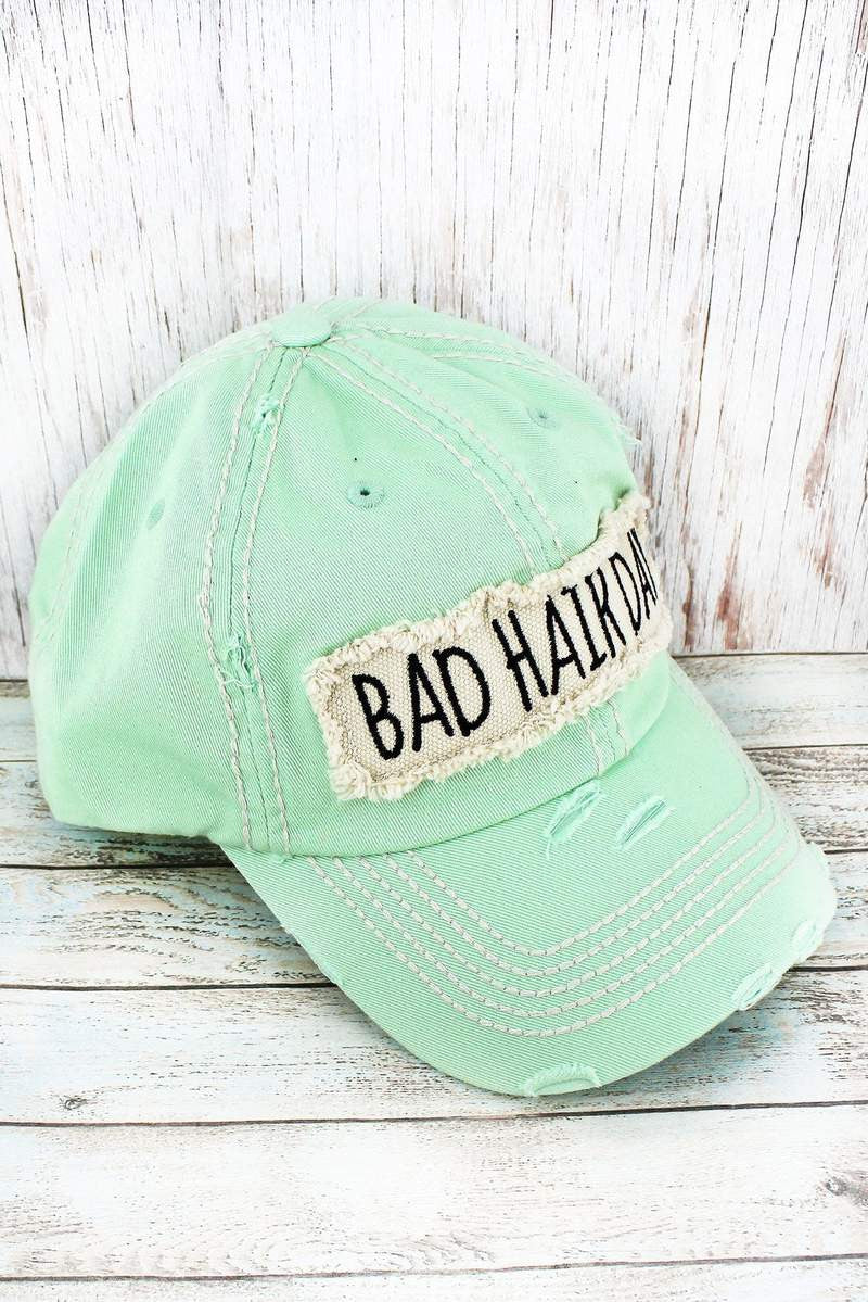 Mint green cap with 'Bad Hair Day' patch on a wooden surface
