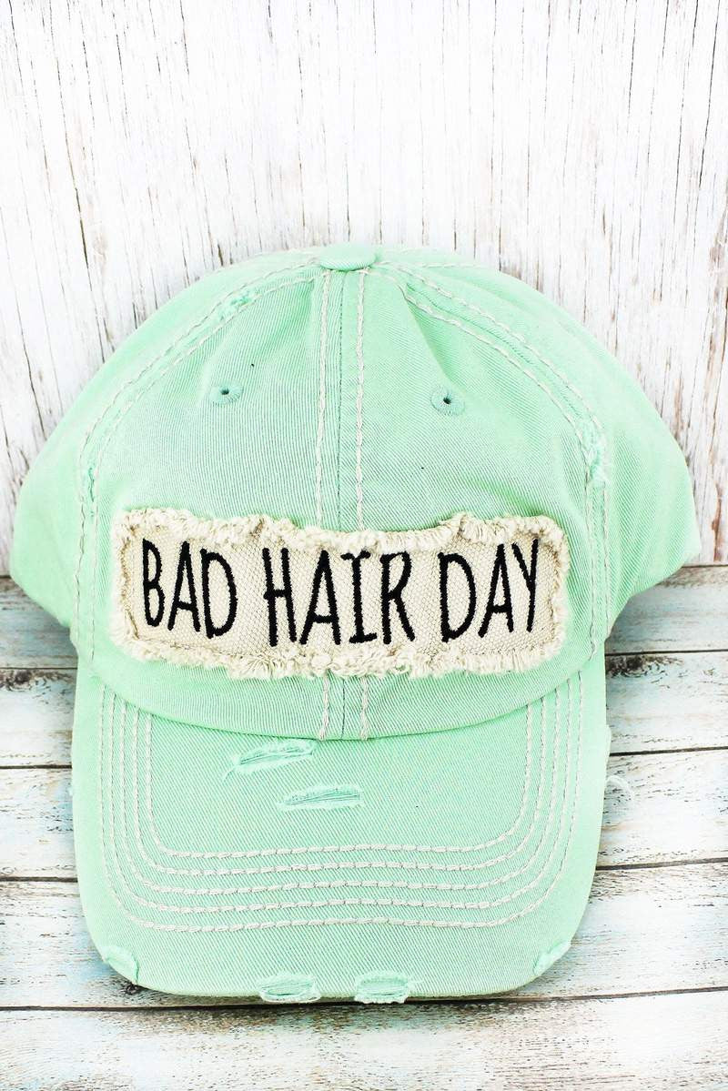 Mint green cap with 'Bad Hair Day' patch on a wooden surface