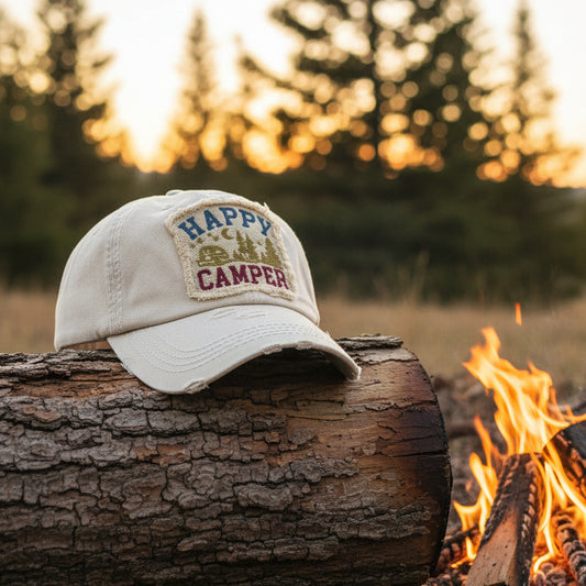 Beige cap with 'Happy Camper' text and graphics on a wooden background