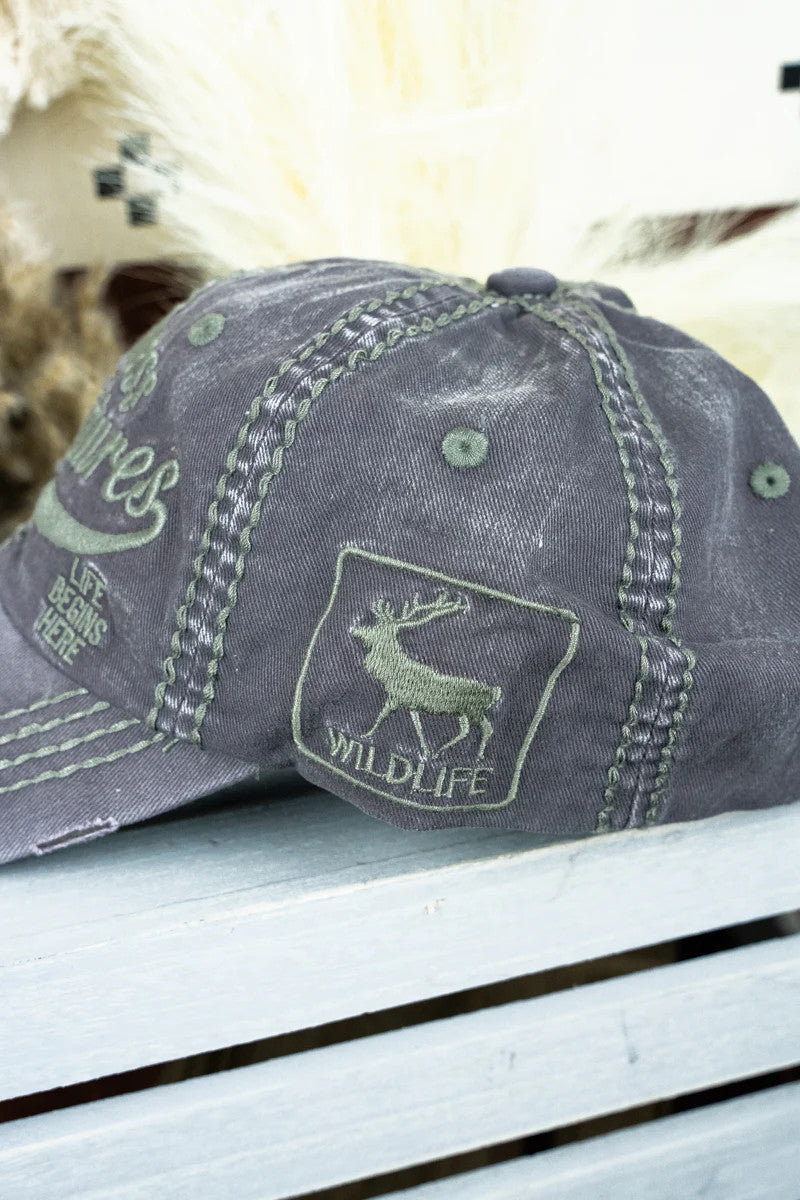 Gray cap with a deer emblem and 'Wildlife' text on a wooden surface