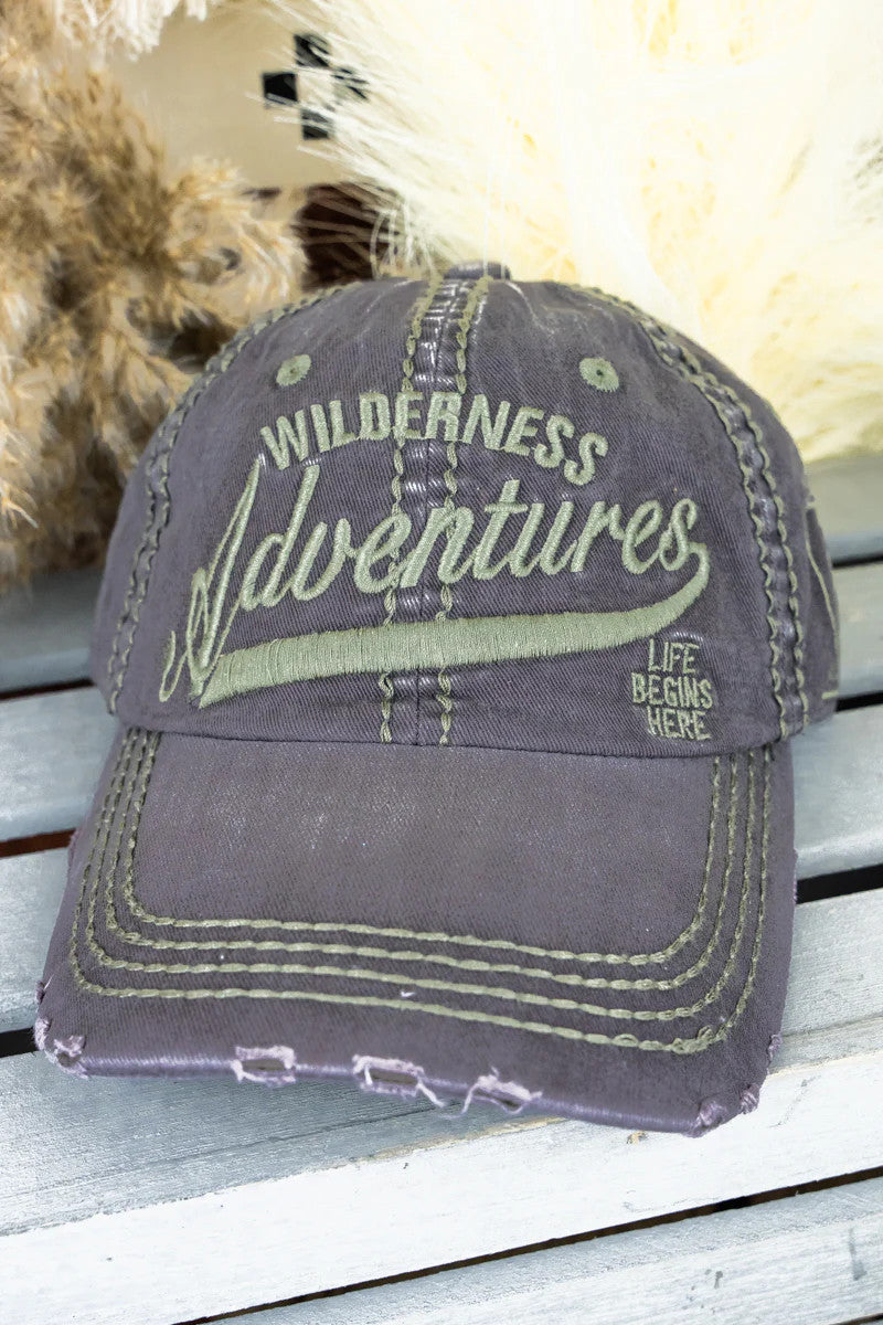 Gray cap with 'Wilderness Adventures' text on a wooden surface